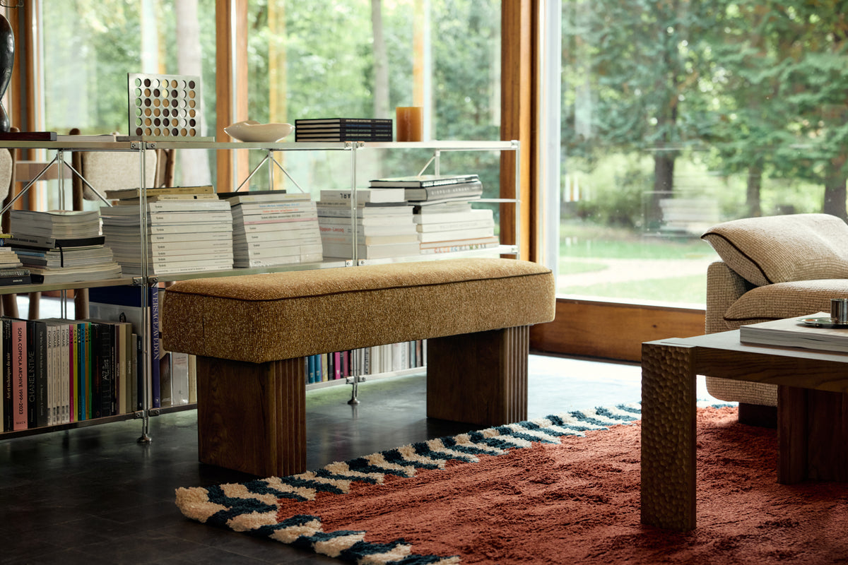 banc Ambery en tissu chiné ocre et piètement bois cannelé devant la bibliothèque