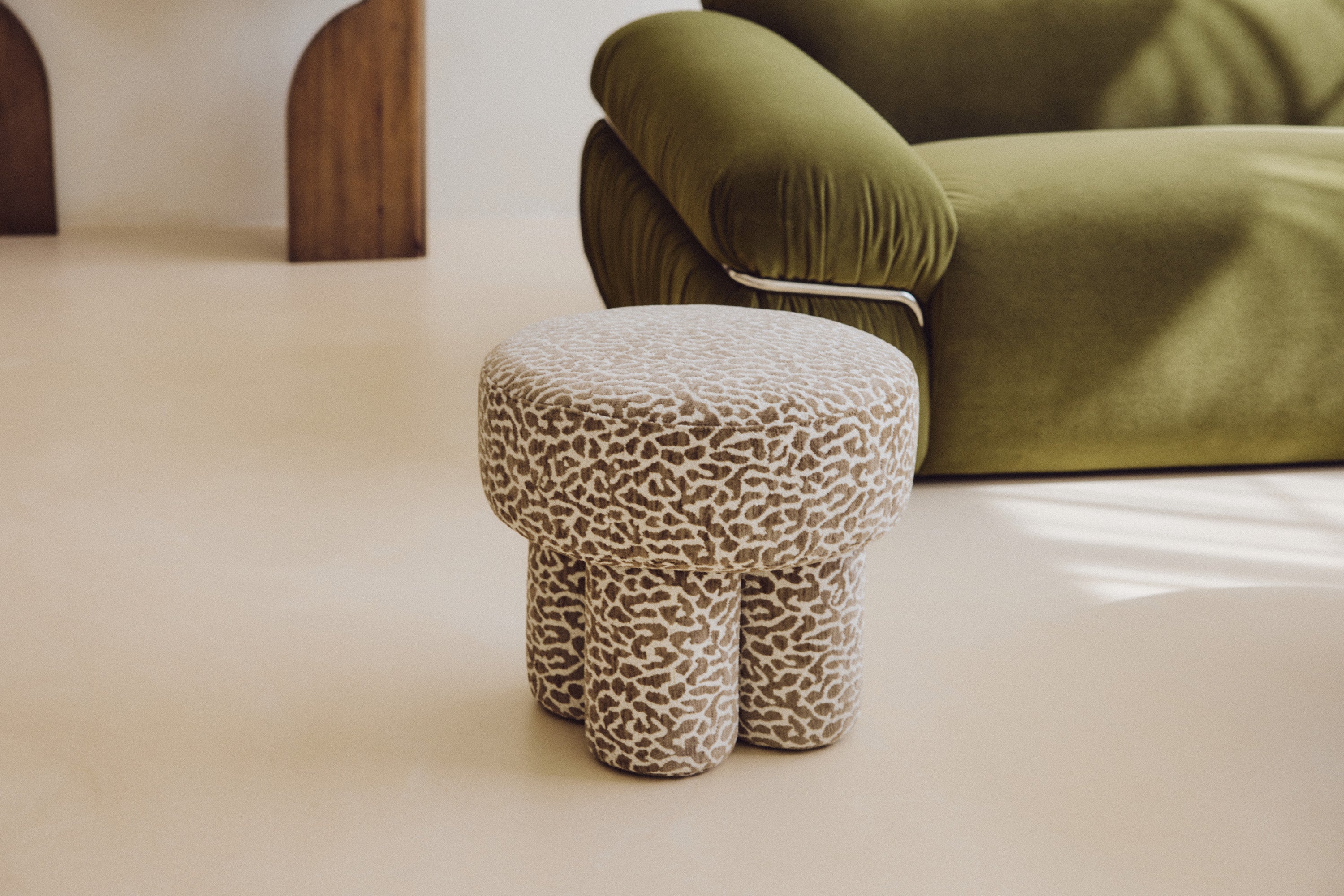 Pouf Corinthe - NV GALLERY - polyester motif léopard marron - au pied d'un canapé velours vert