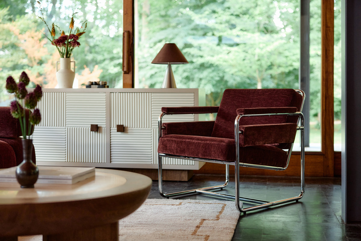 fauteuil Kyle bordeaux et buffet Archi laqué crème dans un salon vitré sur forêt
